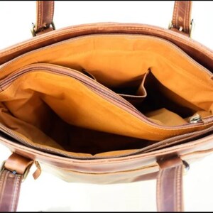 May include: Open view of a brown leather tote bag with multiple compartments. The bag has two handles and a shoulder strap. The interior is lined with a tan fabric and features a zippered pocket and several open pockets. The bag is made of a distressed leather.