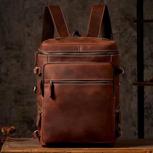 May include: A brown leather backpack with multiple pockets and buckles. The backpack has a large main compartment and several smaller pockets on the front and sides.
