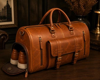 May include: A tan leather duffel bag with a dedicated side compartment for shoes. The bag features a top zip closure, two sturdy handles, a front pocket with buckle straps, and two vertical zipped pockets on the sides of the front compartment.