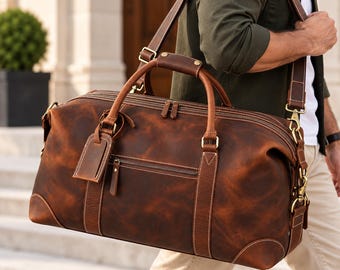 May include: A large brown leather duffel bag featuring dual top handles, a detachable shoulder strap, brass-toned metal hardware, a zippered front pocket, and a matching leather luggage tag attached to the side handle.
