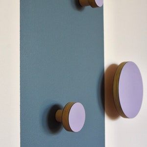 May include: Three wooden wall hooks with a light purple finish. The hooks are mounted on a wall with a white and blue striped background.