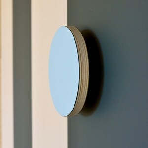 Puede incluir: Un espejo de pared redondo de color azul claro con un marco de madera. El espejo está montado en una pared con rayas blancas y grises.