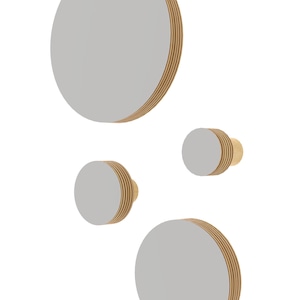 Könnte beinhalten: Satz mit vier runden Wandhaken aus Holz mit hellgrauer Oberfläche. Die Haken sind in verschiedenen Größen und in versetzter Anordnung angeordnet.