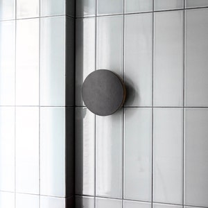Puede incluir: Primer plano de una pared de azulejos blancos con una lámpara redonda negra montada en la pared. Un mostrador rojo con un borde de madera está debajo de la pared.