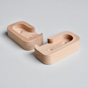 May include: Two unfinished wooden wall mounts with a curved shape and two holes. The mounts are designed to hold a shelf or other object.
