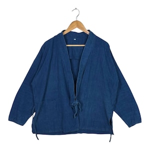 Pode incluir: Casaco azul estilo quimono com mangas compridas, pendurado num cabide de madeira. O casaco tem um fecho de laço na cintura e dois bolsos. O tecido parece ser uma mistura texturizada de algodão ou linho.