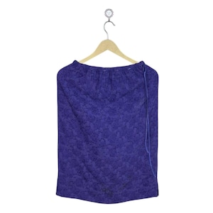 May include: A dark purple skirt with a floral lace design, suspended on a wooden hanger. The skirt features a drawstring waist and a straight cut. The material seems lightweight, ideal for warmer climates.