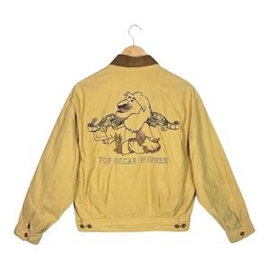 Könnte beinhalten: Eine gelbe Cordjacke mit braunem Cordkragen. Auf der Rückseite der Jacke befindet sich ein gesticktes Bild eines Löwen mit dem Text "TOP OSCAR WINNER".