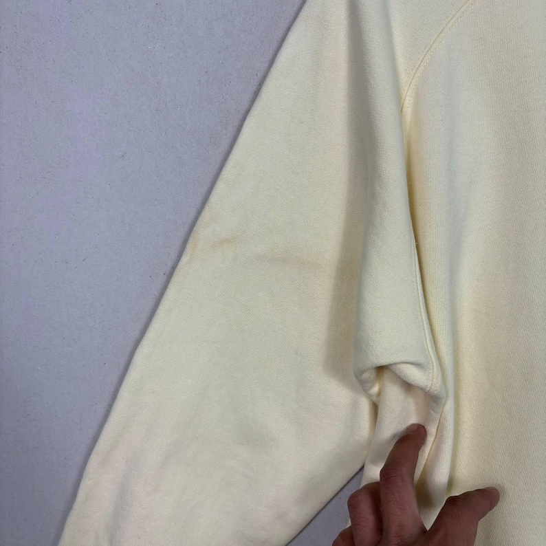 Pode incluir: Close-up de uma manga de camisola amarela p&aacute;lida. A manga tem uma ligeira descolora&ccedil;&atilde;o na parte superior do bra&ccedil;o. O tecido parece ser um material macio e tricotado. O bra&ccedil;o est&aacute; dobrado ao n&iacute;vel do cotovelo.