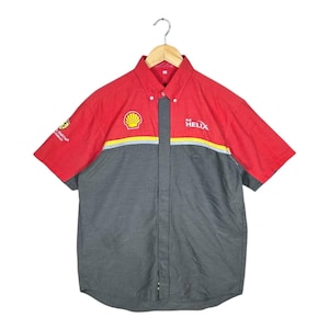 Puede incluir: Una camisa de trabajo de manga corta roja y gris con el logotipo de Shell y el texto "Helix" en la parte delantera. La camisa tiene un cuello abotonado y un bolsillo en el pecho izquierdo.