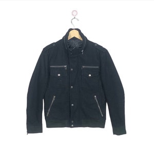 Könnte beinhalten: Eine schwarze Reißverschlussjacke mit Stehkragen und mehreren Taschen. Die Jacke hat einen Knopfverschluss und einen gerippten Saum.