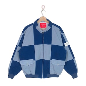 May include: A blue and light blue checked jacket with a zip fastening and a small logo patch on the sleeve. The jacket has two pockets on the front and a ribbed hem.