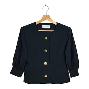 May include: Black jacket with three-quarter sleeves and gold-coloured buttons. The jacket has a round neckline and is hanging on a wooden hanger. The label reads "Givenchy".