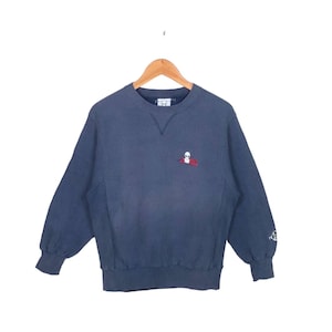 May include: A dark blue sweatshirt with a small embroidered alien graphic on the front. The sweatshirt has a crew neck and long sleeves.