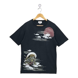 May include: Black t-shirt with a Japanese-inspired design. The shirt features a red sun, white clouds, and a detailed illustration of a mythical creature. The design is printed on the front of the shirt.