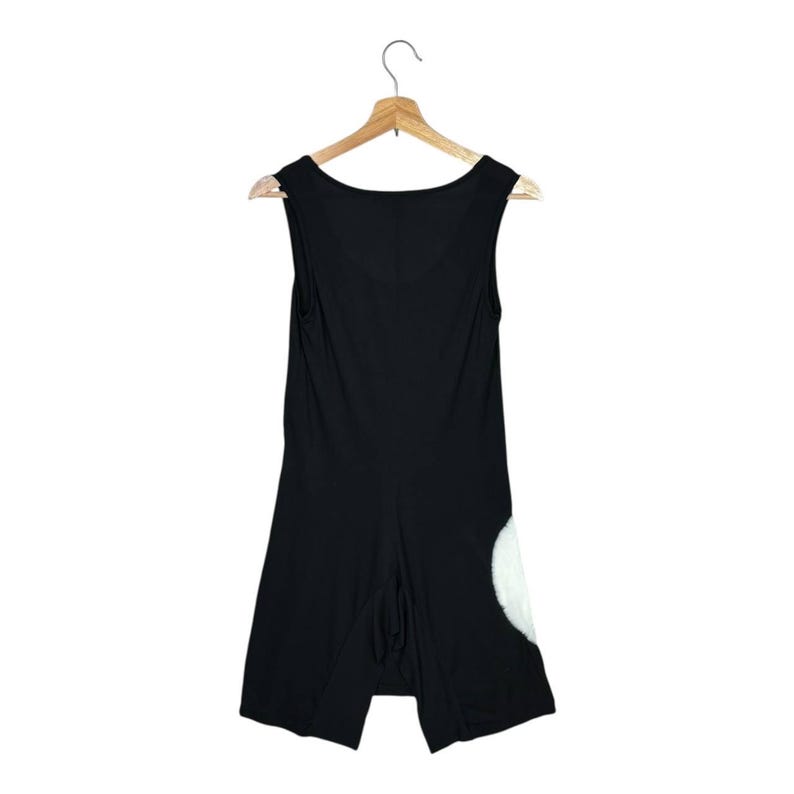 May include: Black sleeveless romper with a scoop neck, hanging on a wooden hanger. The romper features a white, fluffy design on the lower right side. The garment has a split-leg design.