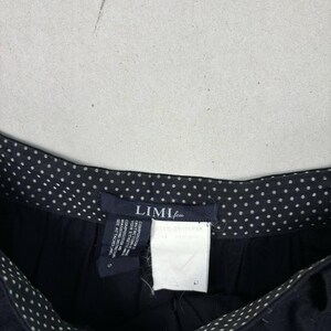 Op de afbeelding: Close-up van een zwarte broek met een witte stippelrand. De broek heeft een label met de tekst "LIMI feu" en bevat wasvoorschriften. De broek is maat S.