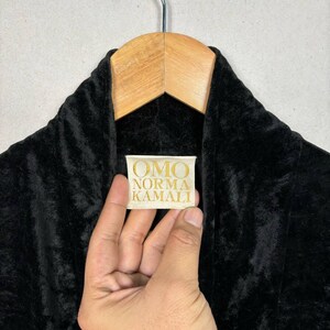 Op de afbeelding: Een zwarte fluwelen badjas met een gouden label waarop "OMO NORMA KAMALI" staat.