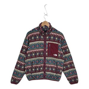 May include: A long-sleeve fleece jacket featuring a maroon, teal, and cream geometric pattern. The jacket has a full-length front zipper, a stand-up collar, two lower zippered pockets, and a solid maroon chest pocket with The North Face logo.