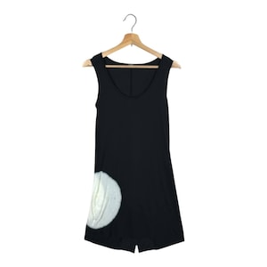May include: Black sleeveless romper with a scoop neckline, hanging on a wooden hanger. A large, white, textured design is on the lower left side of the romper. The romper is made of a soft, flowing fabric.