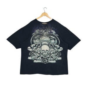 Może przedstawiać: Czarny T-shirt z nadrukiem graficznym czaszki otoczonej różami, diamentami i ozdobnymi wzorami. Na koszulce nadrukowany jest tekst "Unleashed".