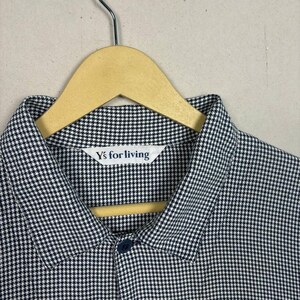 May include: A black and white checkered shirt with a button-down collar, hanging on a wooden hanger. The shirt has a small label that reads "Y's for living". The fabric has a small, repeating pattern.