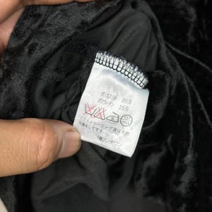Op de afbeelding: Een zwart stoffen label met witte tekst die de stofsamenstelling beschrijft: 85% polyester en 15% polyurethaan. Het label bevat ook wasinstructies in het Japans.