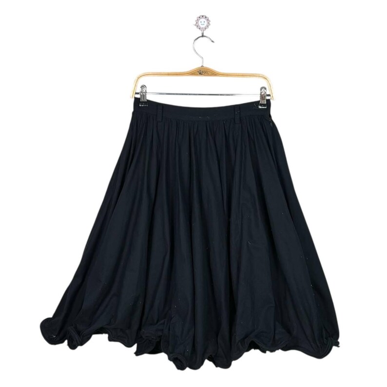 Op de afbeelding: Een zwarte rok met een uniek, volumineus silhouet. De rok hangt aan een houten kleerhanger tegen een witte achtergrond. De stof lijkt een zacht, vloeiend materiaal te zijn, met een geplooid taille en een ballonzoom.