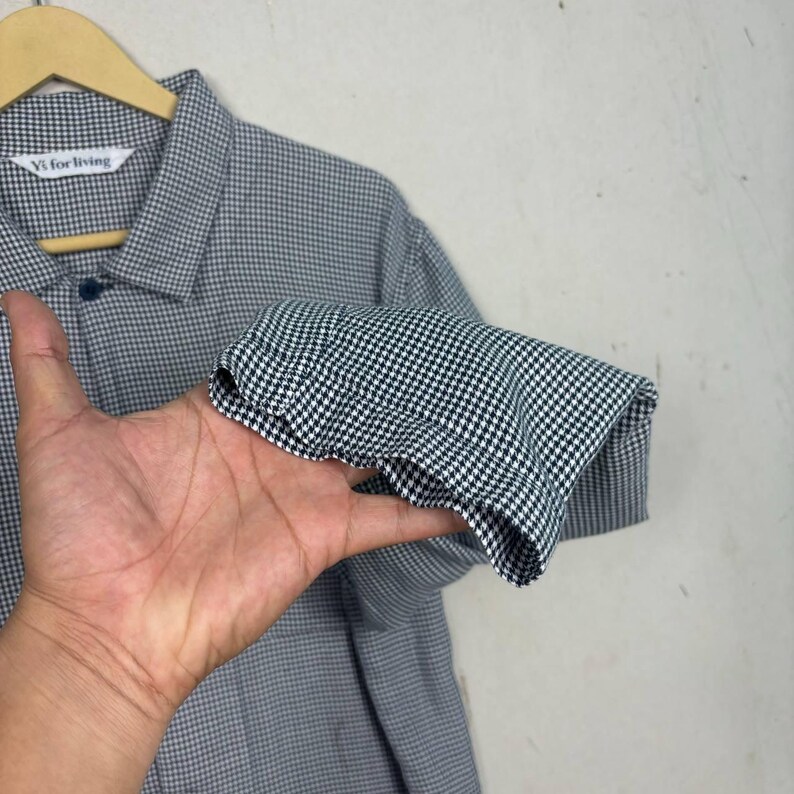 May include: A black and white checkered button-down shirt with a collar and long sleeves. The shirt is hanging on a wooden hanger. The label reads "Vi for living".