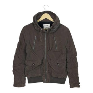 May include: Brown bomber jacket with a hood, two front pockets, and two chest pockets. The jacket has a zipper closure and the text "SKY BOMBER" on the label.