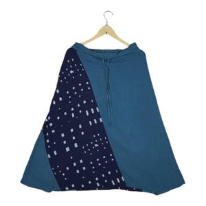 May include: A teal skirt with a wide, flowing design. It features a navy blue panel on the left, decorated with a white dotted pattern. The skirt hangs from a wooden hanger, showing its shape and drawstring waist. (Approx. 100 cm)