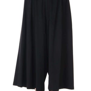 Op de afbeelding: Zwarte broek met wijde pijpen en een taille met trekkoord. De broek heeft een los, vloeiend ontwerp en is gemaakt van een effen zwarte stof. De broek wordt gecombineerd met zwarte schoenen.