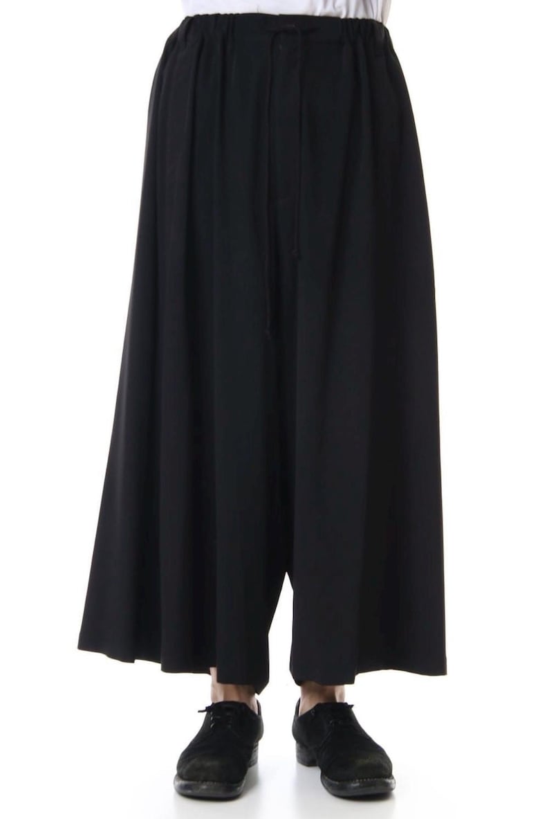Op de afbeelding: Zwarte broek met wijde pijpen en een taille met trekkoord. De broek heeft een los, vloeiend ontwerp en is gemaakt van een effen zwarte stof. De broek wordt gecombineerd met zwarte schoenen.