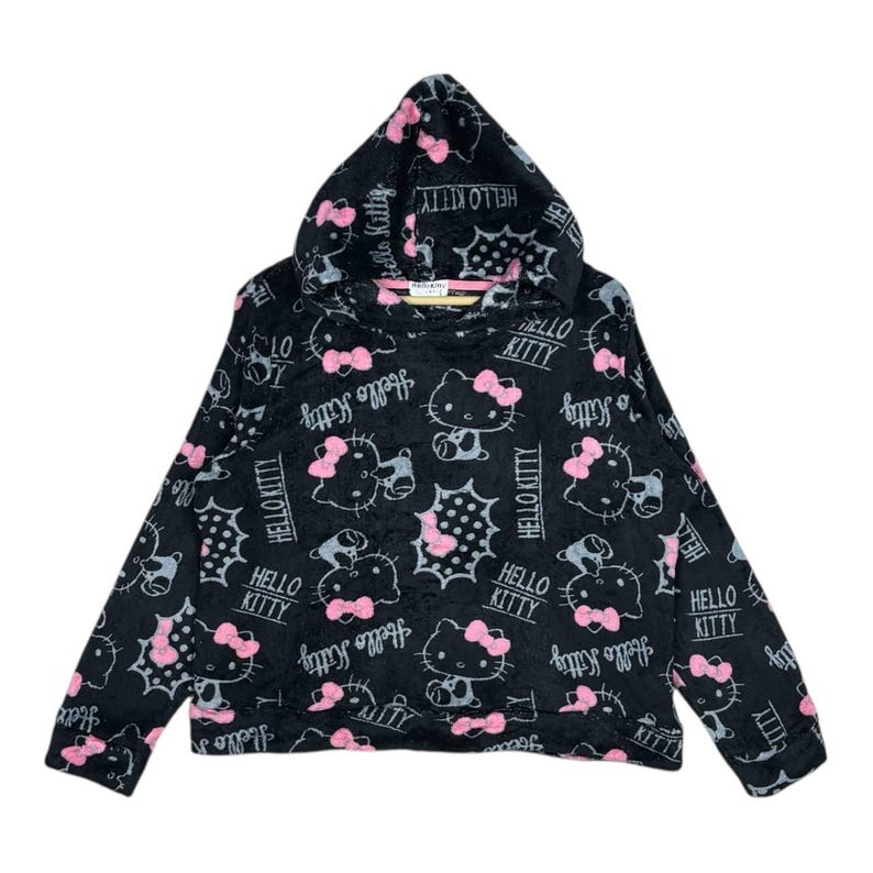 Puede incluir: Sudadera con capucha negra con un patr&oacute;n repetido de personajes de Hello Kitty con lazos rosas y las palabras "Hello Kitty" en blanco. La sudadera tiene una capucha con cord&oacute;n y mangas largas.