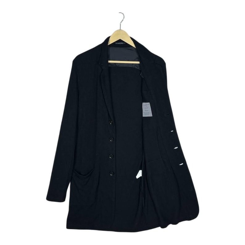 Może przedstawiać: Czarny długi płaszcz z zapięciem na guziki z przodu i dwiema przednimi kieszeniami. Płaszcz wisi na drewnianym wieszaku na białym tle. Płaszcz jest otwarty, odsłaniając podszewkę i małą metkę.