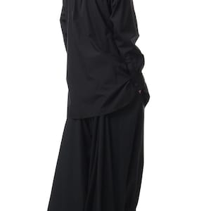 Op de afbeelding: Zwart ensemble bestaande uit een lange mouwen overhemd met knopen en een wijde broek. Het overhemd heeft een klassieke kraag en manchetten met knopen. De broek heeft een vloeiend, oversized ontwerp. De schoenen zijn van leer met een lage hak.