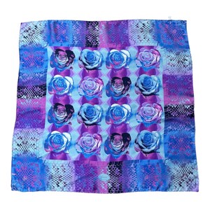May include: Square silk scarf with a floral rose pattern in shades of blue, purple, and white. The scarf has a snakeskin print border in blue and purple. The scarf is a square shape.