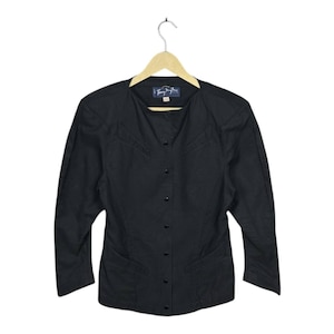 May include: A black button-down jacket with long sleeves, hanging on a wooden hanger. The jacket has a round collar and two front pockets. The label reads "Tommy Hilfiger".
