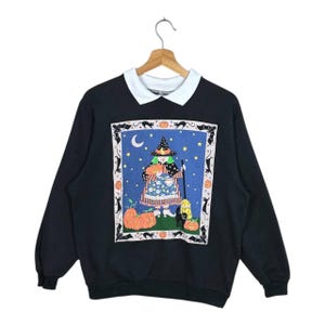 Puede incluir: Sudadera negra de Halloween con cuello blanco. La parte delantera presenta un gráfico colorido de una bruja sosteniendo una calabaza, con calabazas y gatos negros. El fondo es un cielo nocturno estrellado. Una parte superior divertida y festiva para la temporada espeluznante.