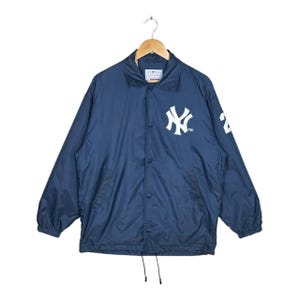 May include: Navy blue nylon jacket with the New York Yankees logo in white on the chest. The jacket has a button-up front, a drawstring hem, and the number 2 on the right sleeve. The jacket is hanging on a wooden hanger.