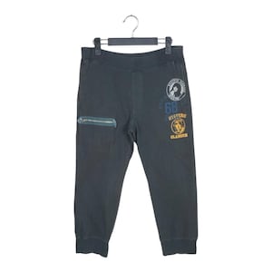 Puede incluir: Pantalones de chándal verde oscuro con un bolsillo con cremallera en la pierna izquierda y parches bordados en la pierna derecha. Los parches muestran la cara de una mujer, el número 68, la palabra "HYSTERIC", la cara de un hombre y la palabra "GLAMOUR".