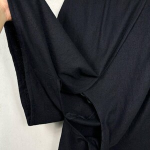 Op de afbeelding: Close-up van een zwart kledingstuk, mogelijk een shirt of jas, met een getextureerde stof. De stof is gevouwen en onthult de binnenkant en naden. Het kledingstuk lijkt gemaakt van een zacht, donker materiaal.