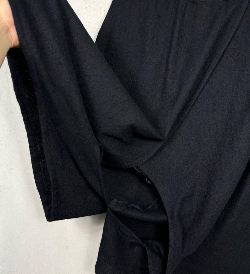 Op de afbeelding: Close-up van een zwart kledingstuk, mogelijk een shirt of jas, met een getextureerde stof. De stof is gevouwen en onthult de binnenkant en naden. Het kledingstuk lijkt gemaakt van een zacht, donker materiaal.