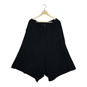 Op de afbeelding: Zwarte shorts met wijde pijpen, hangend aan een houten hanger. De shorts hebben een taille met trekkoord en een knoopsluiting. De stof lijkt een zacht, vloeiend materiaal te zijn.