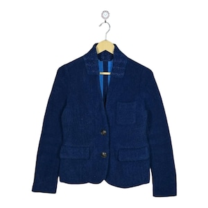 Puede incluir: Un blazer azul oscuro con dos bolsillos delanteros y dos botones oscuros. El blazer está colgado de una percha de madera. El interior del blazer es de color azul claro.