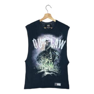 May include: A black sleeveless t-shirt featuring a graphic print of a cowboy on horseback with the text THE LAST OUTLAW. The shirt includes a WWE Authentic Wear logo on the collar and a small rectangular WWE WEAR patch at the bottom hem.