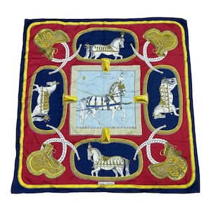 Puede incluir: Pañuelo cuadrado de seda con fondo rojo y borde azul marino. El pañuelo presenta un diseño central de un carruaje tirado por caballos e ilustraciones de caballos enmarcadas en azul marino. Acentos dorados y un borde amarillo completan el diseño.