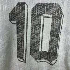 May include: Close-up of a white jersey featuring a large, distressed number 10 on the back. The number is grey with a geometric pattern. The jersey has a subtle, repeating pattern.