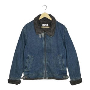 May include: Blue denim jacket with a gray faux fur collar and lining. The jacket has a zipper closure, two front pockets, and gray trim on the cuffs and hem. The jacket is hanging on a wooden hanger.