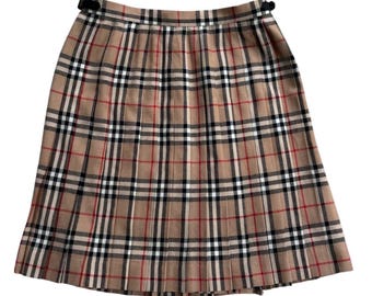 May include: A pleated skirt in a classic plaid pattern, featuring a tan base with black, red, and white stripes. The skirt has a tailored fit and a button closure at the waist. The skirt is a timeless piece.
